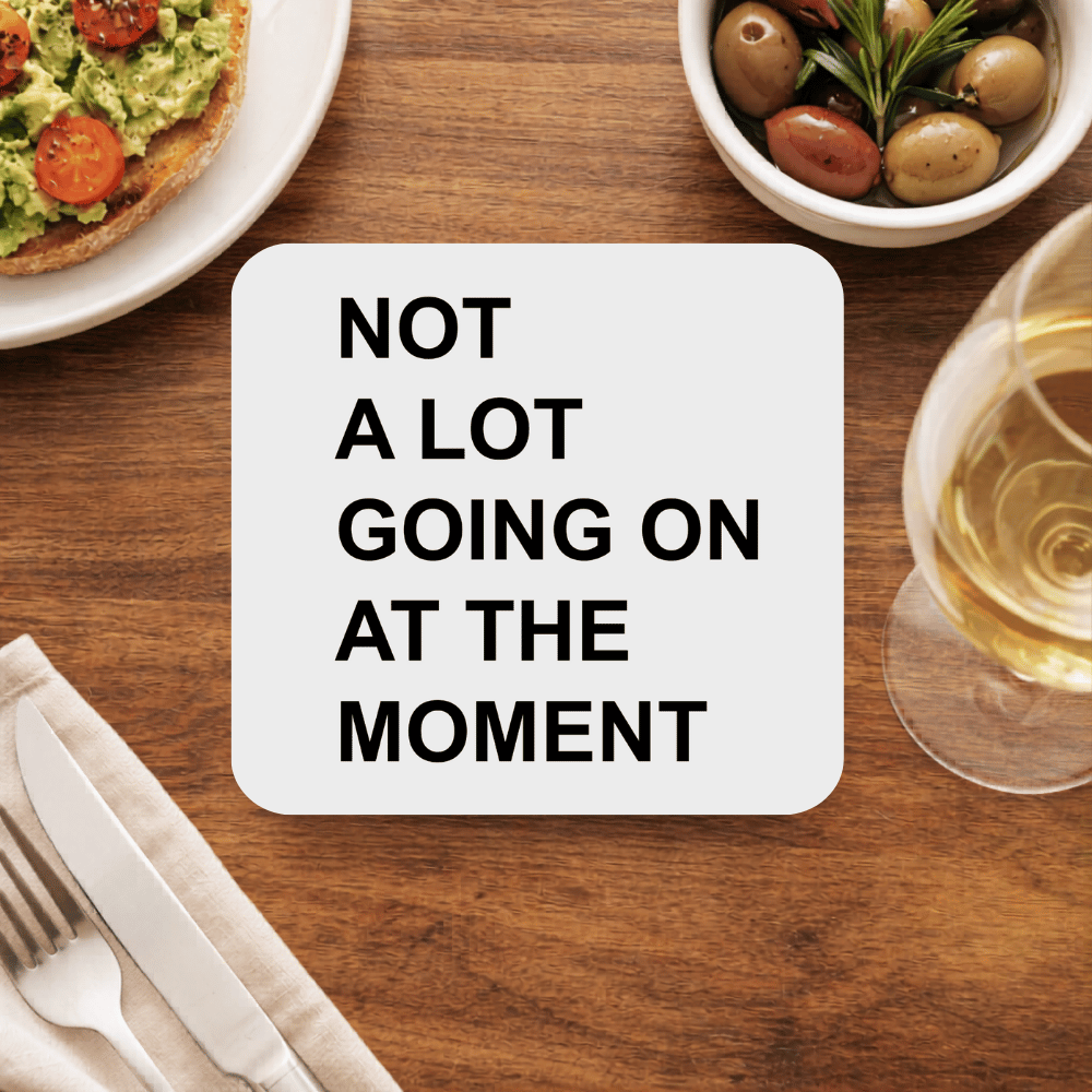 Taylor Swift Not A Lot Going On coaster in bold black block type on a light grey square beside avocado toast and white wine