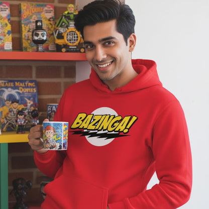 Person wearing a red 'Bazinga!' hoodie holding a mug with a colorful design, standing in front of a shelf with toys and books. The Big Bang Theory Bazinga Hoodie.