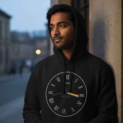 Man wearing a black hoodie with a clock design leaning against a wall. The Banyan Tee Pink Floyd Time Hoodie.