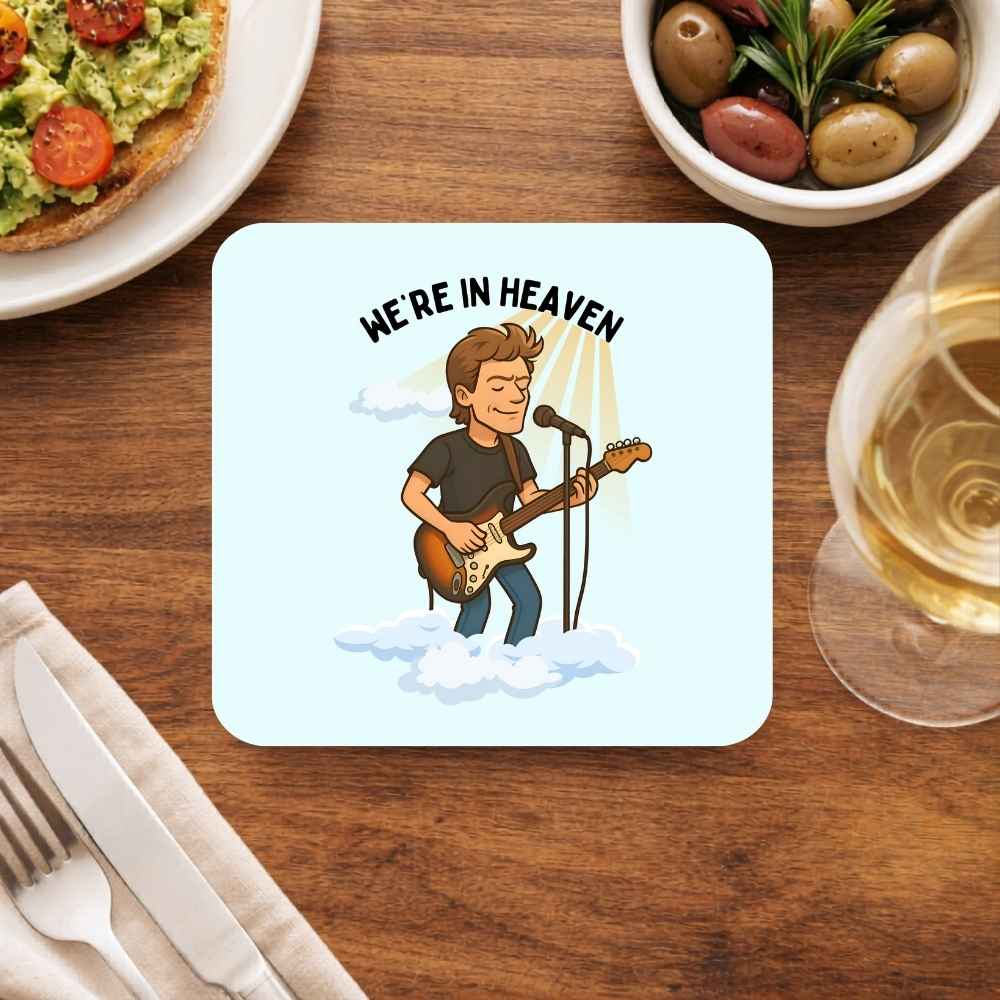 Coaster with a cartoon of a man playing guitar and text 'We're in Heaven' on a table with food and drink. Bryan Adsms