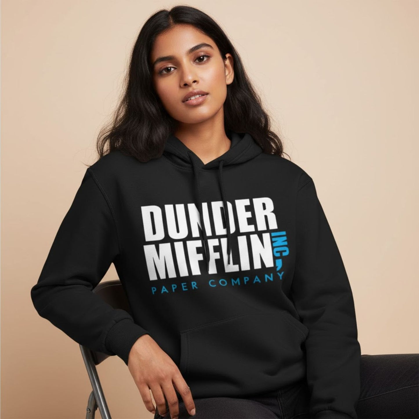 Person wearing a black hoodie with 'Dunder Mifflin Inc Paper Company' text on a beige background