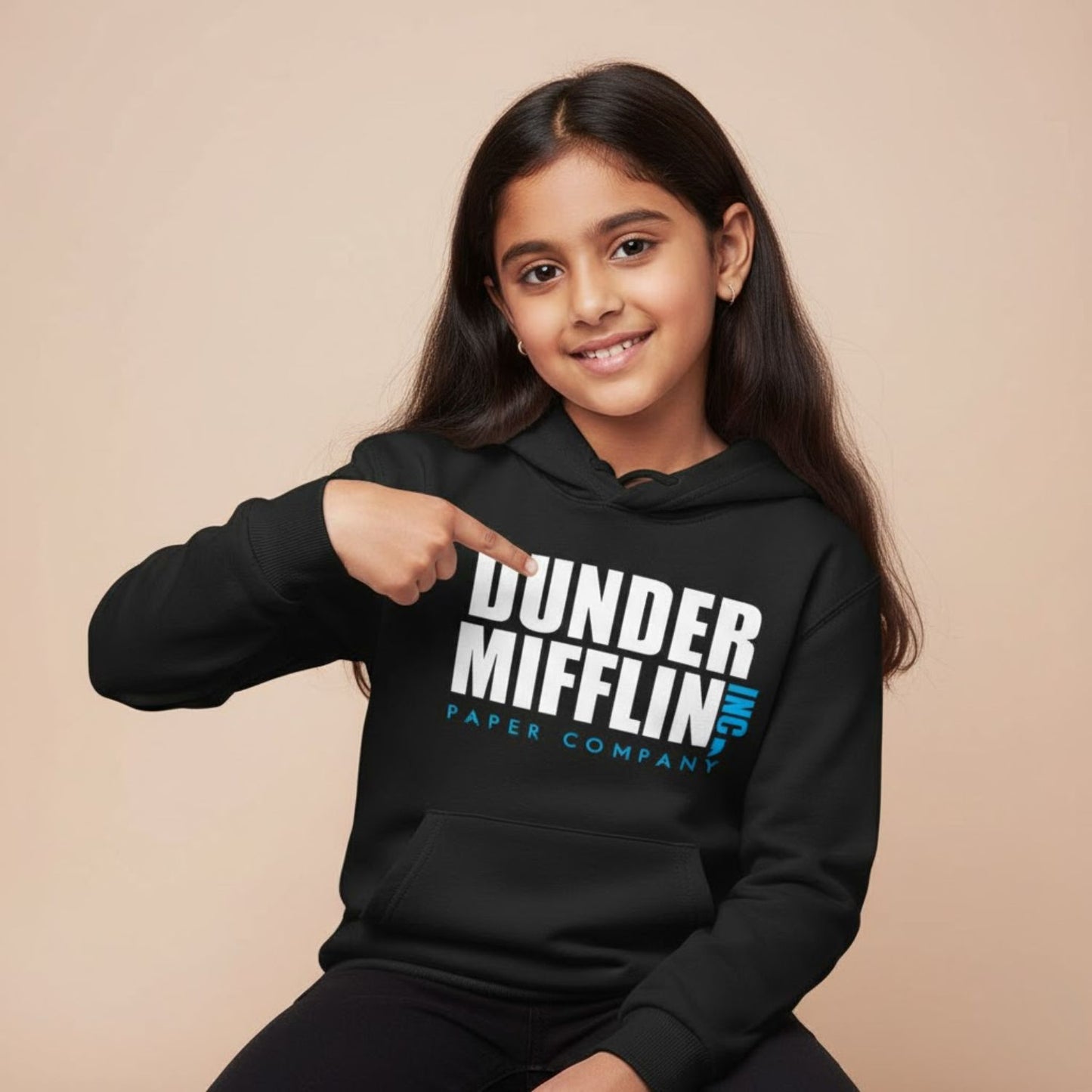 Child wearing a black hoodie with 'Dunder Mifflin Paper Company' text, pointing to the hoodie.