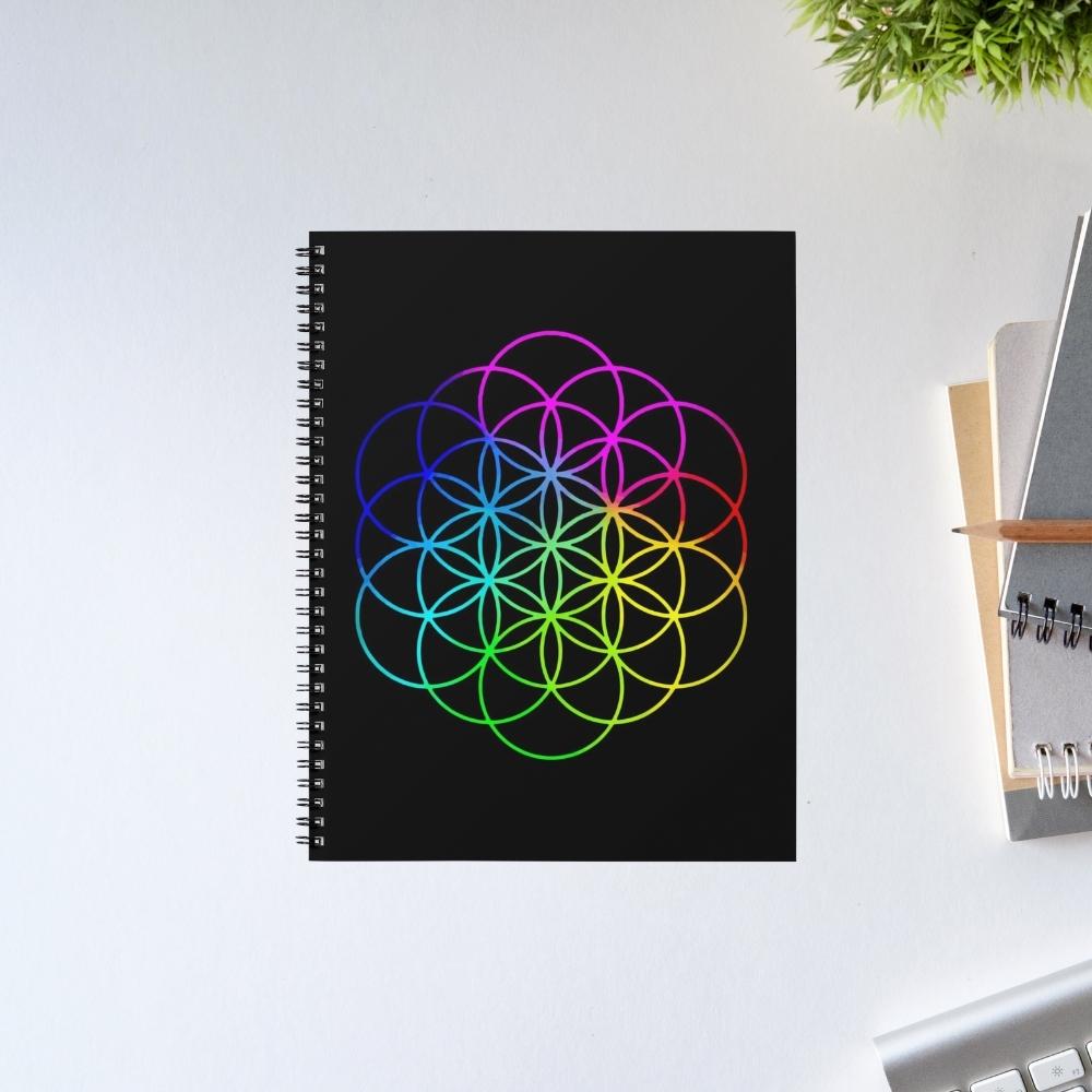 Spiral-bound notebook with a colorful geometric design on a white surface. Coldplay The Banyan Tee