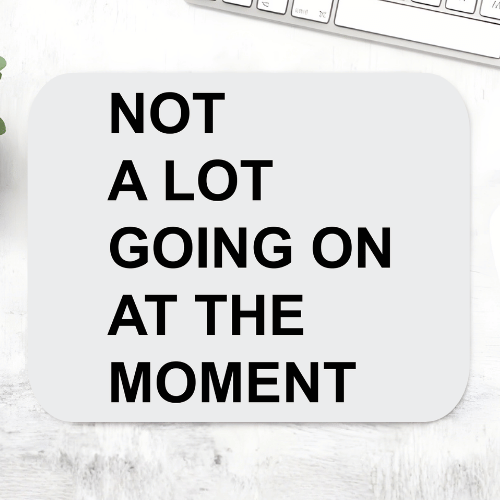 Taylor Swift Not A Lot Going On mousepad with bold black text 'Not a lot going on at the moment' on a light grey rounded mouse pad – non-slip desk mouse mat, The Banyan Tee