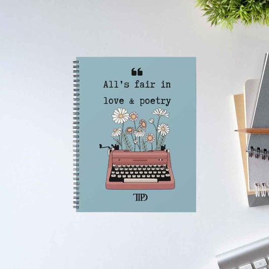 Taylor Swift Love & Poetry spiral notebook with the line 'All's fair in love & poetry' above a pink typewriter sprouting daisies, on a dusty blue cover – unruled notepad diary, The Banyan Tee