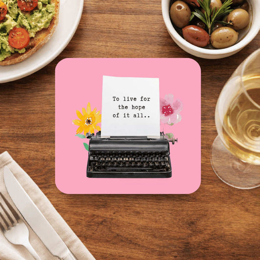 Taylor Swift coaster with a black vintage typewriter, a yellow and a pink flower and a page typed To live for the hope of it all, on bright pink